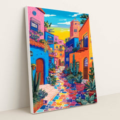 This artwork shows a vibrant, colorful street with blue, orange, and pink buildings, potted cacti, and a mosaic tile walkway, in a white frame.
