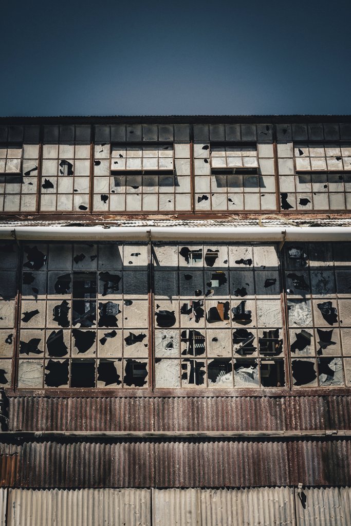 Alfo Medeiros - A captivating image of an abandoned factory showcasing broken windows and a rusty facade.