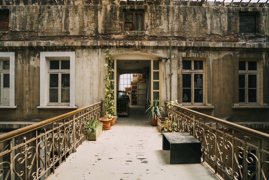 Sami TÜRK - An abandoned building exterior with plants and vintage railings in an urban setting.