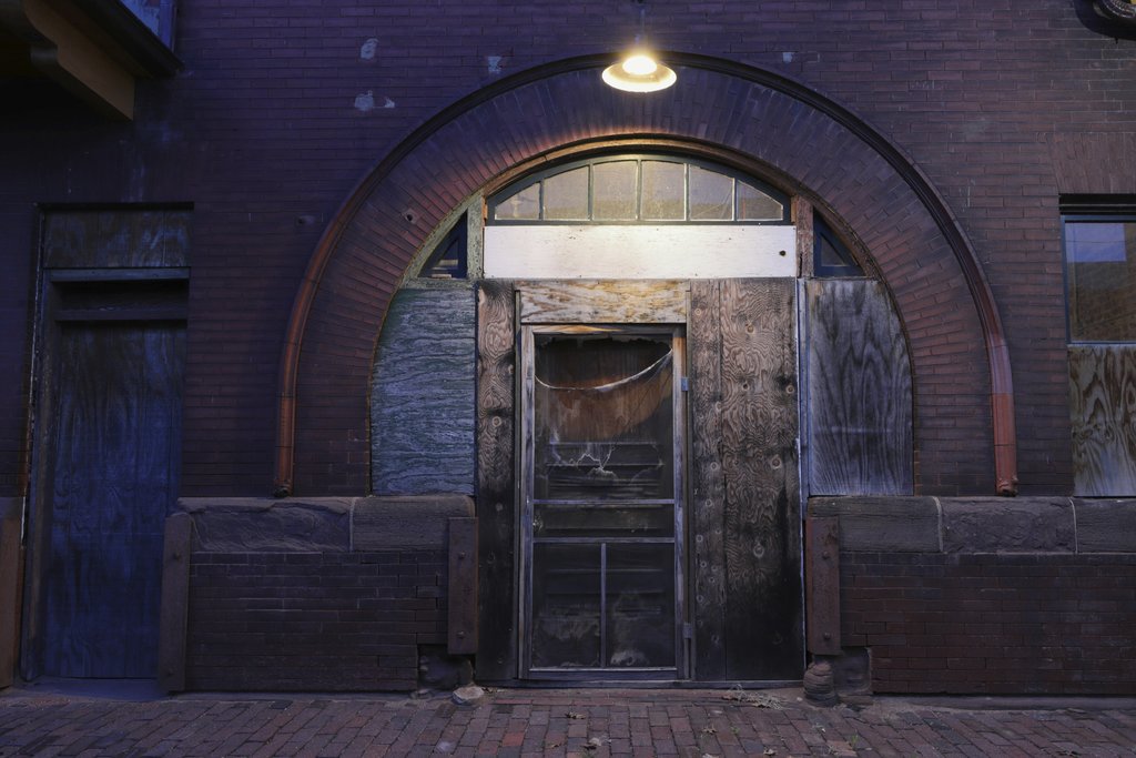 Scott Platt - Dramatic image of an abandoned building's entryway featuring a wooden door and arched brick facade.