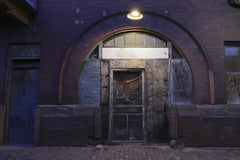 Scott Platt - Dramatic image of an abandoned building's entryway featuring a wooden door and arched brick facade.