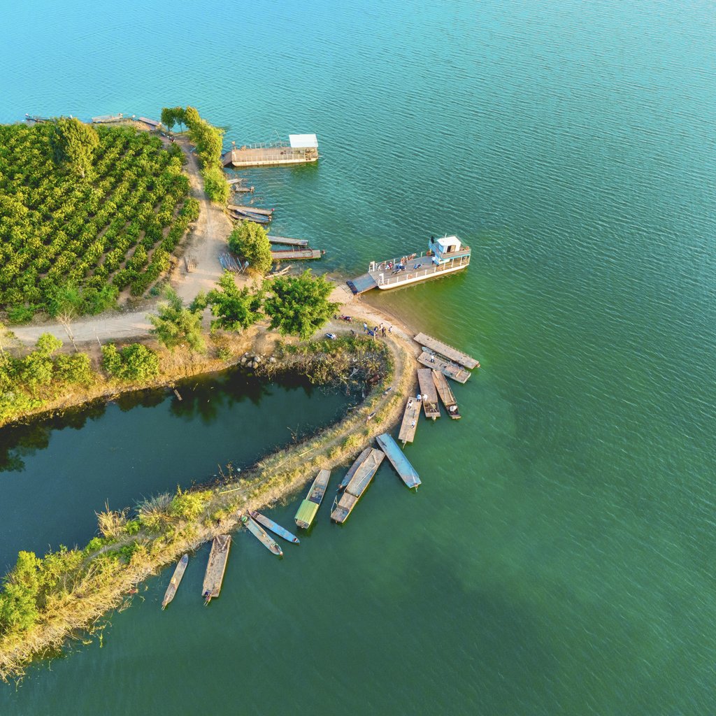 Duy Nguyen - Aerial shot of boats on a shore with lush vegetation by a serene lake.