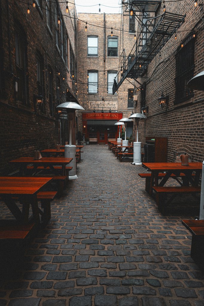 Allen Boguslavsky - Rustic alleyway with string lights and wooden benches, perfect for outdoor dining vibes.