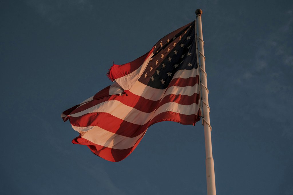 Connor McManus - A vibrant American flag waves proudly on a flagpole, set against a dramatic sky.