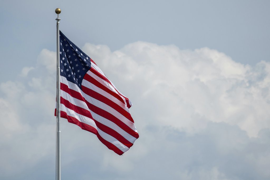 Andrew Patrick Photo - A vibrant American flag waving on a flagpole with a cloudy sky backdrop, symbolizing national pride.