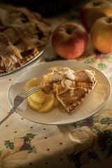 MikeGz - A warm slice of apple pie served on a holiday-decorated table with apples.