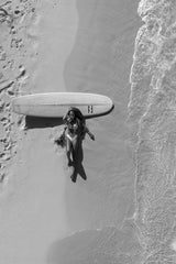 Jess Loiterton - Black and white aerial view of a woman sunbathing by a surfboard on the beach.