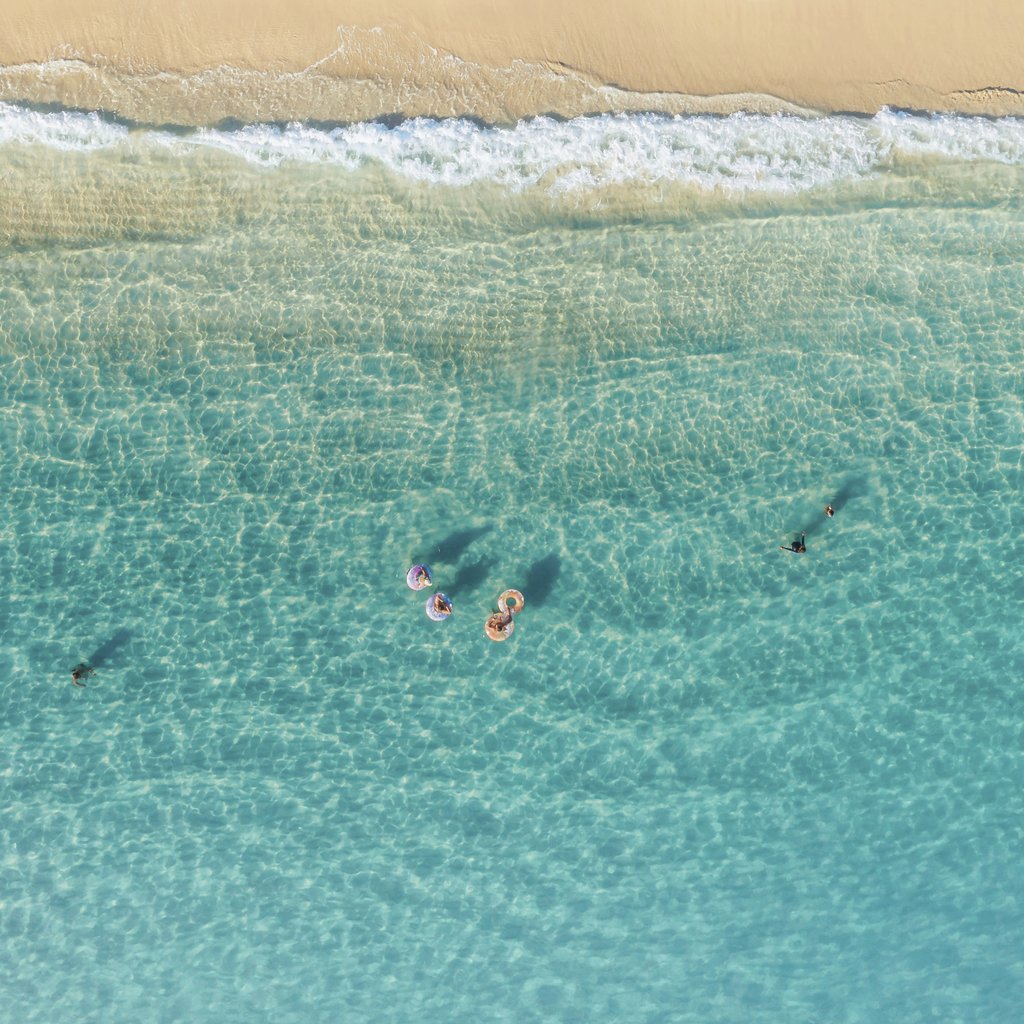Jess Loiterton - A stunning aerial shot of people enjoying swimming in turquoise waters near a sandy beach.