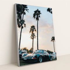 This photo shows a classic black Porsche sports car parked under tall palm trees at sunset, in a silver frame.