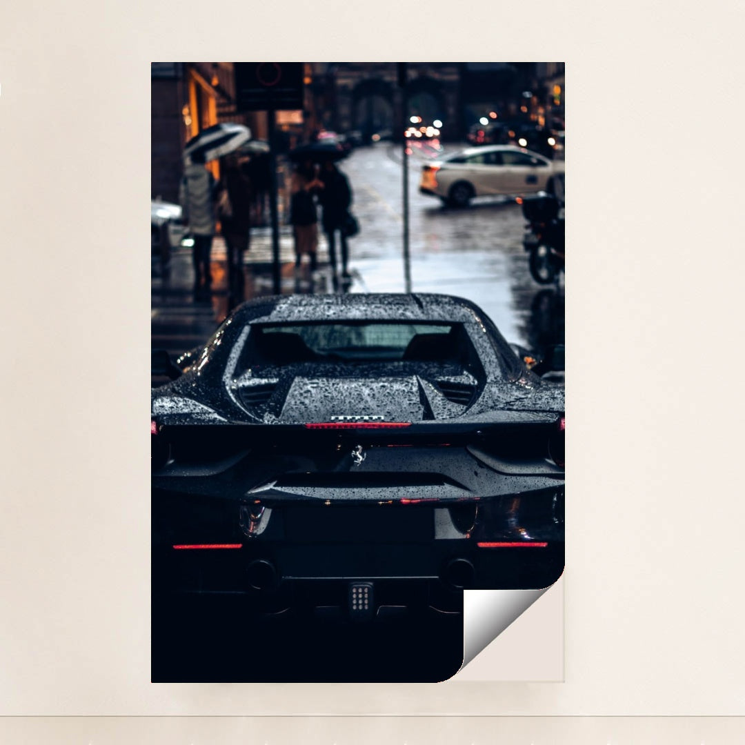This photo shows the rear view of a black Ferrari covered in rain droplets on a wet city street at night, minimalist unframed style.