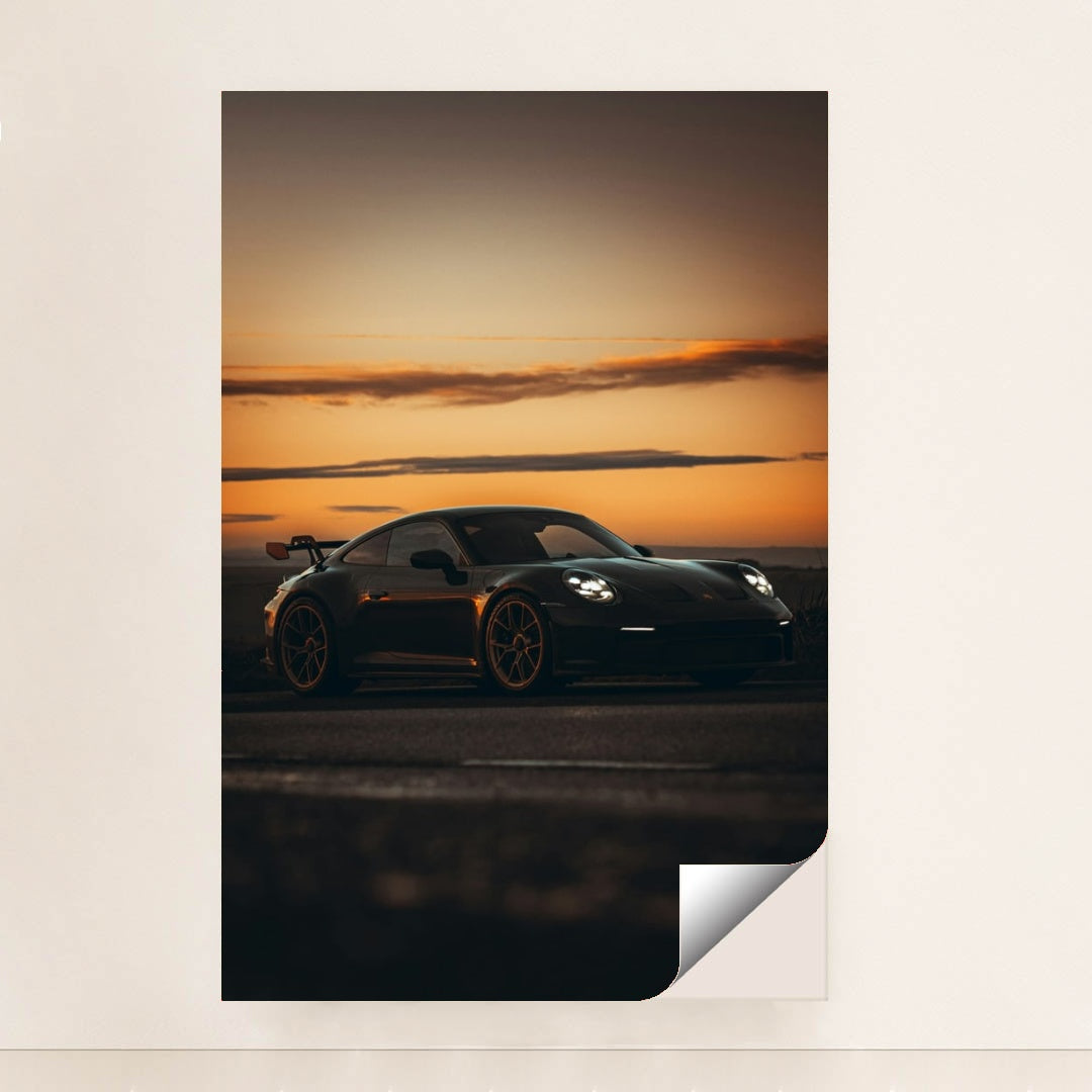 This photo shows a black Porsche sports car with a rear wing parked at sunset, minimalist unframed style.
