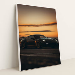This photo shows a black Porsche sports car with a rear wing parked at sunset, in a white frame.