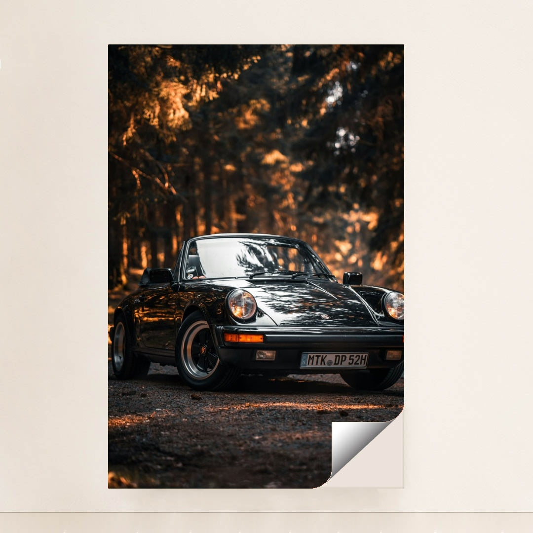 This photo shows a classic black Porsche convertible parked on a forest road with golden sunlight, minimalist unframed style.