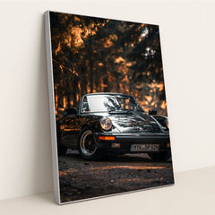 This photo shows a classic black Porsche convertible parked on a forest road with golden sunlight, in a silver frame.