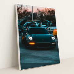 This photo shows a black Porsche 911 with LED headlights at dusk, parked at a car meet with people and vehicles in the background, in a white frame.