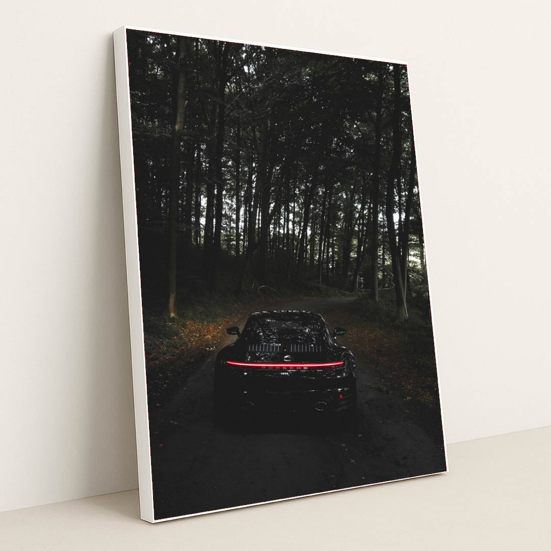 This photo shows the rear of a black Porsche with taillights illuminated, parked on a dark forest road, in a white frame.