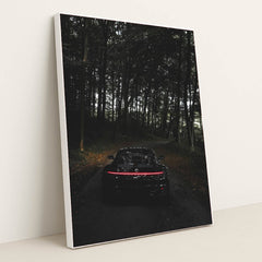 This photo shows the rear of a black Porsche with taillights illuminated, parked on a dark forest road, in a white frame.