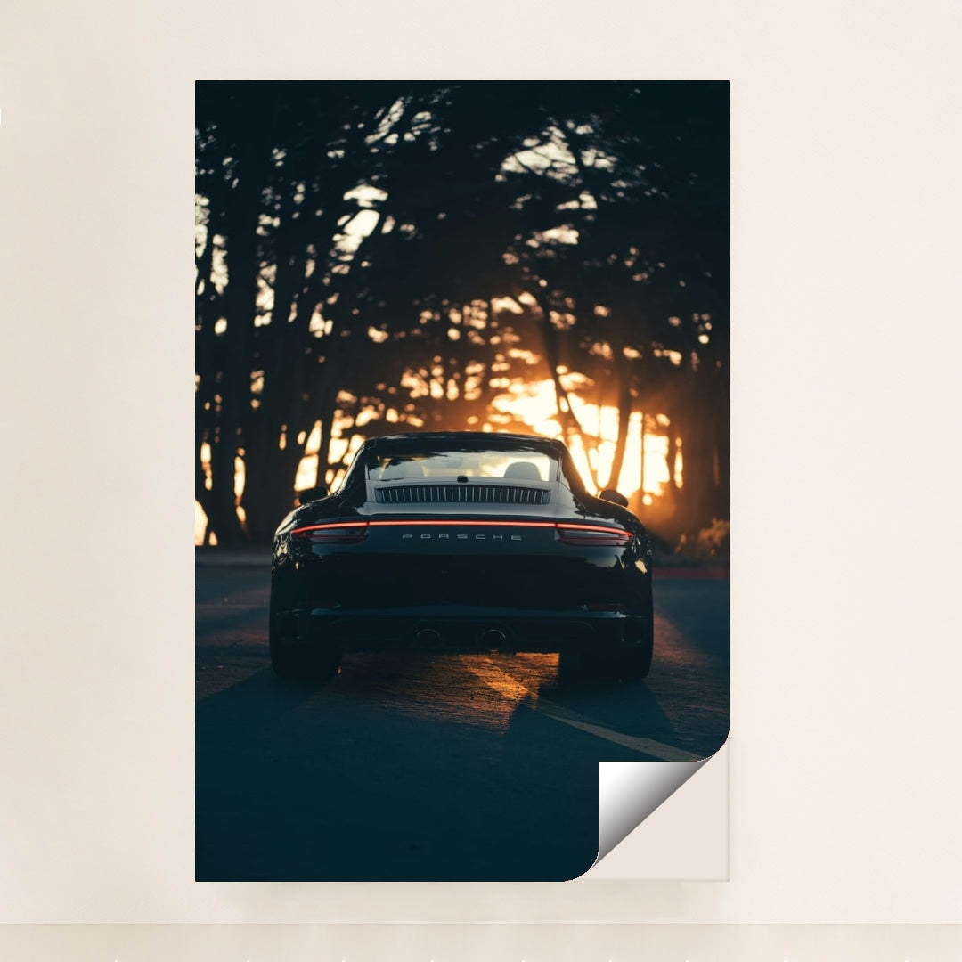 This photo shows the rear view of a black convertible Porsche parked on a tree-lined road at sunset, minimalist unframed style.