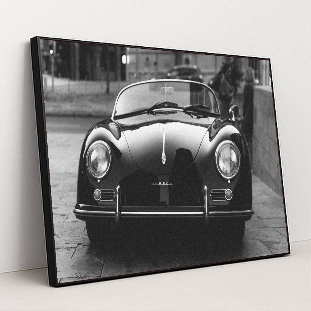 This photo shows a classic black Porsche Speedster convertible parked on a city street in black and white, in a black frame.