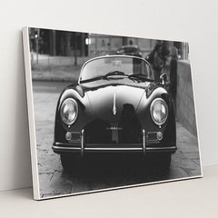 This photo shows a classic black Porsche Speedster convertible parked on a city street in black and white, in a white frame.
