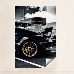 This photo shows the rear side view of a black Porsche GT sports car with gold wheels parked outside a dealership, minimalist unframed style.