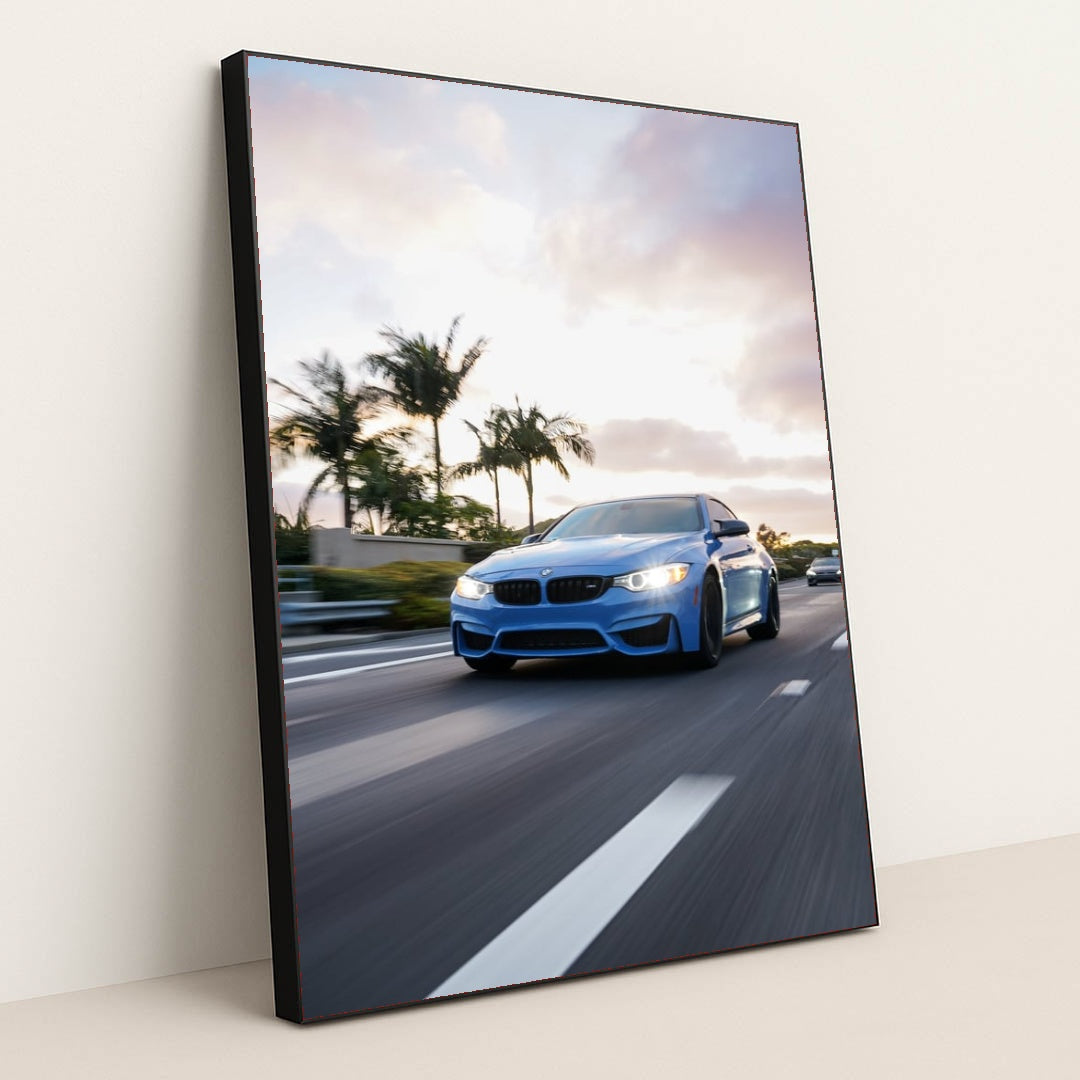 This photo shows a blue BMW driving down a palm-tree-lined highway at sunset, in a black frame.