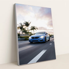 This photo shows a blue BMW driving down a palm-tree-lined highway at sunset, in a silver frame.