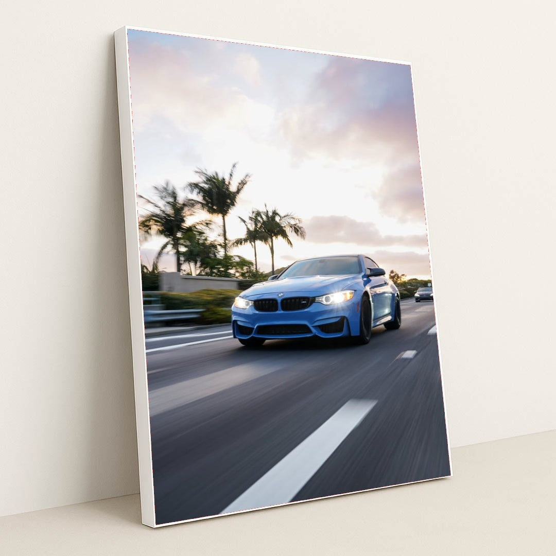 This photo shows a blue BMW driving down a palm-tree-lined highway at sunset, in a white frame.