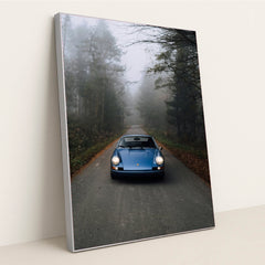 This photo shows a classic blue Porsche 911 parked on an empty forest road in morning mist, in a silver frame.