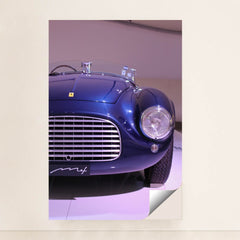 This photo shows the front left side of a blue vintage Ferrari convertible under display lights, minimalist unframed style.