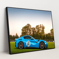 This photo shows a blue Ferrari sports car with racing stripes and the number 171 parked on grass at sunset, in a black frame.