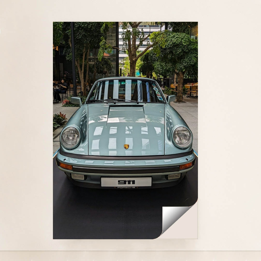 This photo shows a pastel blue classic Porsche 911 coupe on display in a modern indoor courtyard with trees, minimalist unframed style.