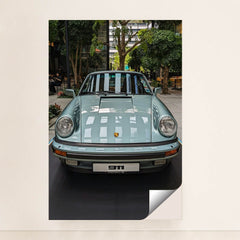 This photo shows a pastel blue classic Porsche 911 coupe on display in a modern indoor courtyard with trees, minimalist unframed style.