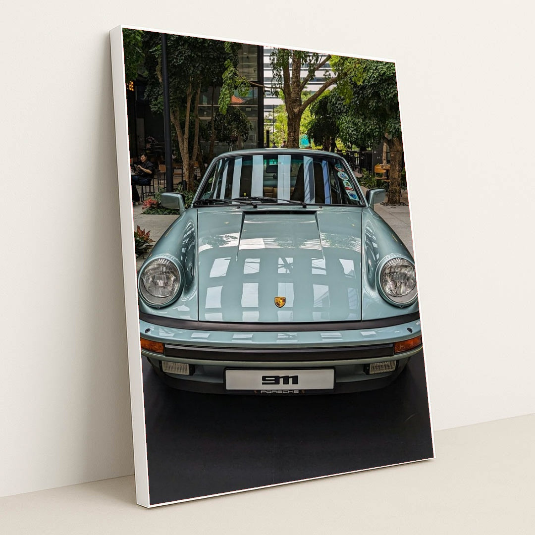 This photo shows a pastel blue classic Porsche 911 coupe on display in a modern indoor courtyard with trees, in a white frame.