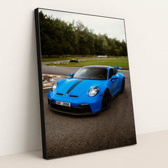 This photo shows a bright blue Porsche 911 GT3 with black racing stripes parked on a curvy racetrack, in a black frame.