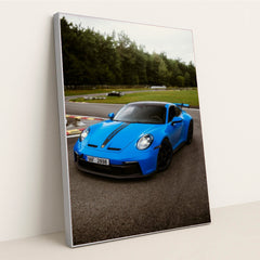This photo shows a bright blue Porsche 911 GT3 with black racing stripes parked on a curvy racetrack, in a silver frame.