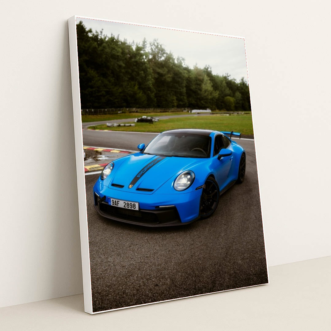This photo shows a bright blue Porsche 911 GT3 with black racing stripes parked on a curvy racetrack, in a white frame.