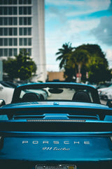 Porsche 911 Turbo Convertible in the City parked in front of a vibrant cityscape with palm trees, showcasing luxury car wall art.