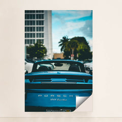 This photo shows the rear view of a blue Porsche 911 Turbo convertible with the top down, parked in a city with palm trees, minimalist unframed style.