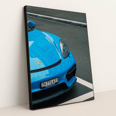 This photo shows the front of a blue Porsche sports car with raindrops, parked on wet pavement, in a black frame.
