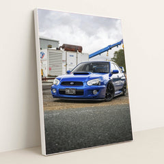 This photo shows a blue Subaru WRX with black wheels parked in an industrial lot, in a white frame.