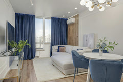 Max Vakhtbovycn - Bright living room with blue curtains, plants, and modern furniture.