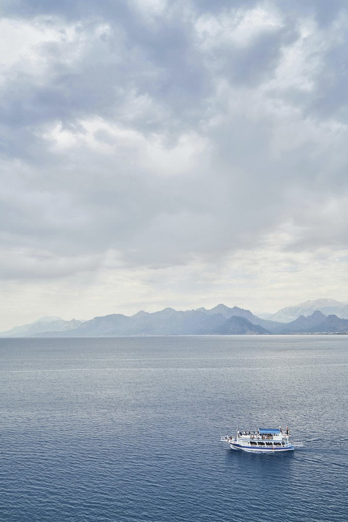 Engin Akyurt - A lone boat sails across a tranquil sea beneath cloudy skies and distant mountains.