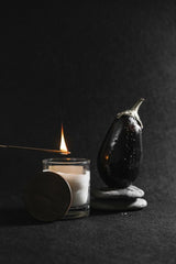 Mikhail Nilov - A minimalist still life featuring a lit candle, an eggplant, and stones on a dark surface.