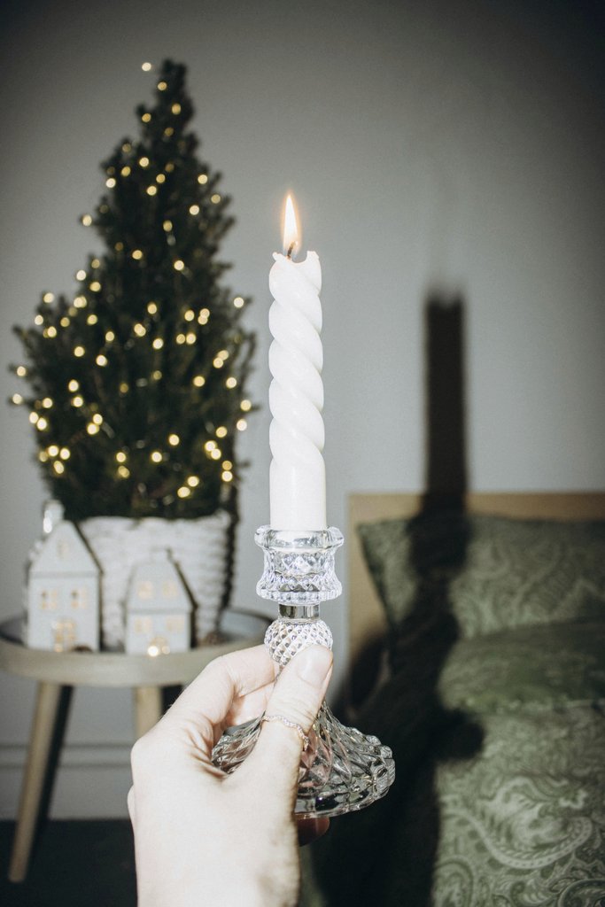 Liudmyla Shalimova - A hand holding a lit candle with a Christmas tree in the background, creating a festive ambiance.