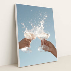 This artwork shows two hands clinking wine glasses with a splash against a clear blue sky, in a white frame.