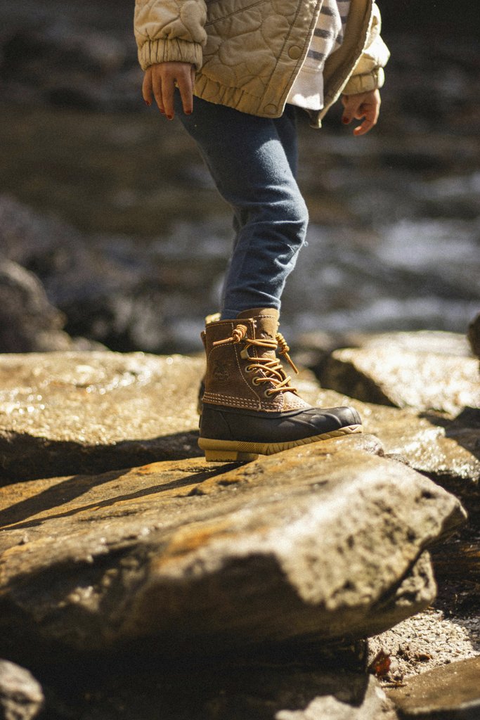 Daniel & Hannah Snipes - A child stands on rocks by a stream in North Carolina, showcasing durable boots.