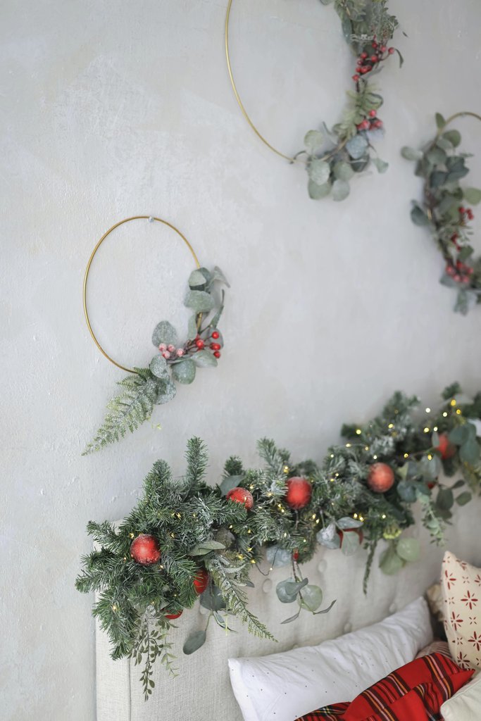Valeria Boltneva - Elegant Christmas wreaths and garland with red accents on a white wall.