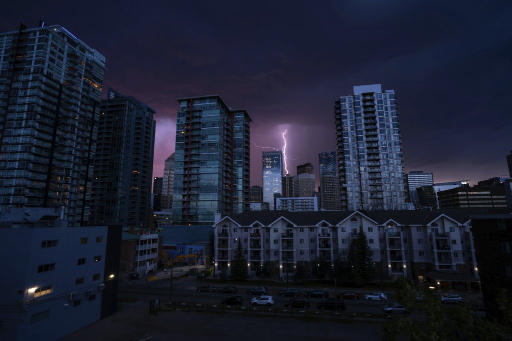 Donovan Kelly - Lightning strikes behind a city skyline at night, highlighting tall skyscrapers under a dramatic sky.