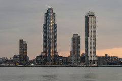 _ Whittington - A tranquil view of New York City skyscrapers at sunset with reflections on the East River.